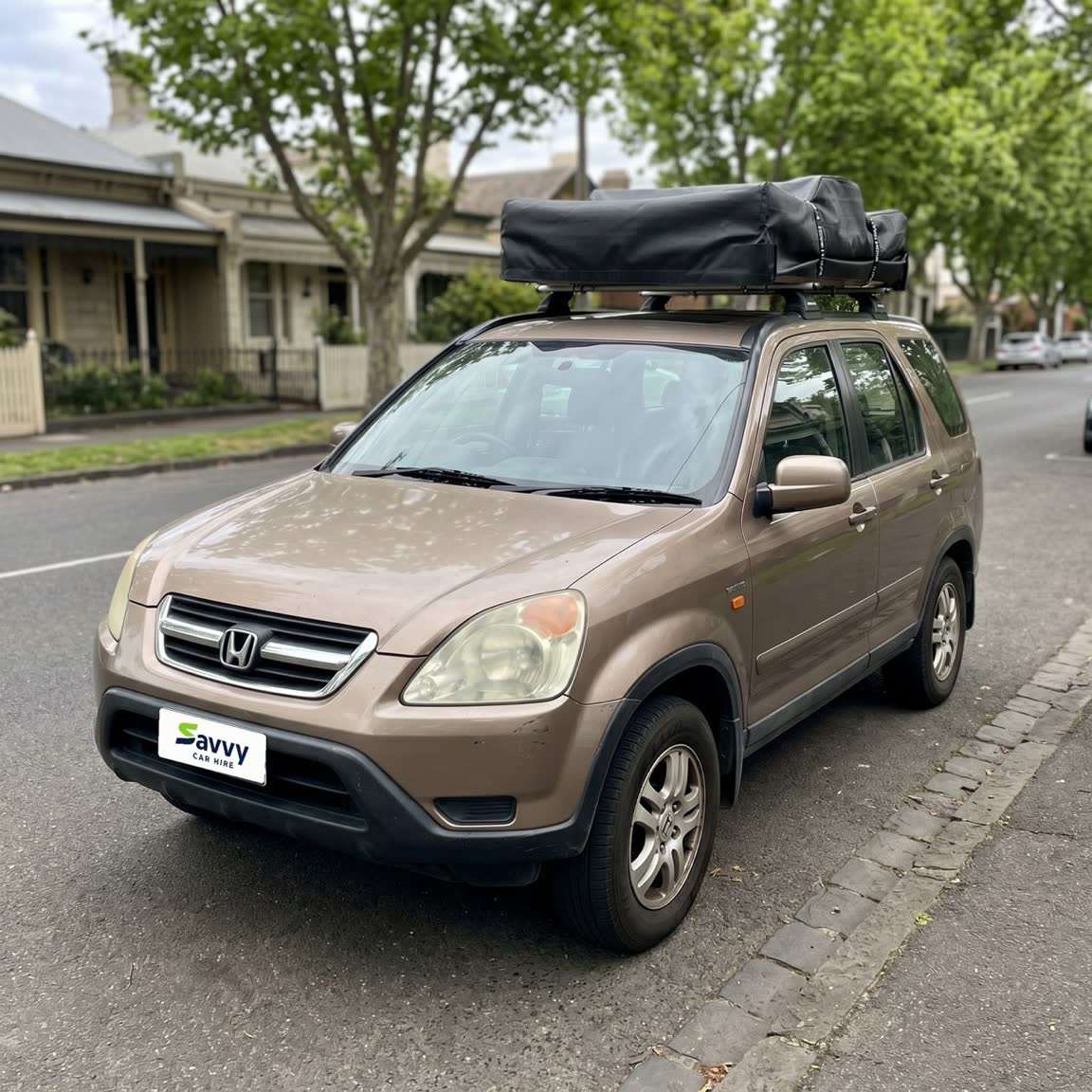 A gold Honda CR-V with a roof bag, one of our fleet cars, parked on a tree-lined Melbourne street